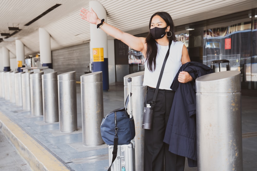 woman wearing a mask hailing for a cab at the airport